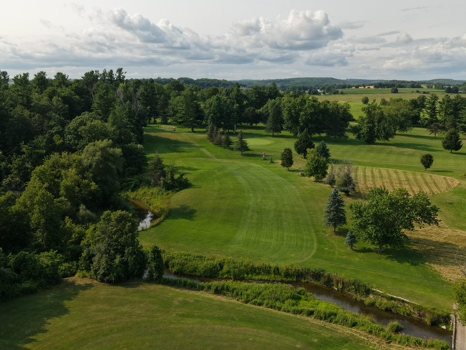 Drone aerial of a tree-lined par 4 with a creek crossing, Southern Ontario golf course, by Fringe & Fescue